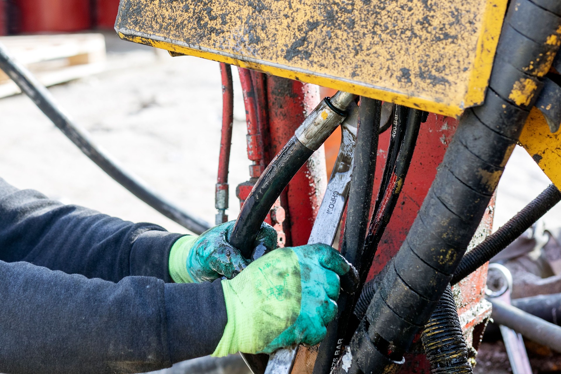 Worker is repairing hydraulic hoses of working machine. Hydraulic machines use liquid fluid power to perform work. Heavy construction vehicles are a common example.