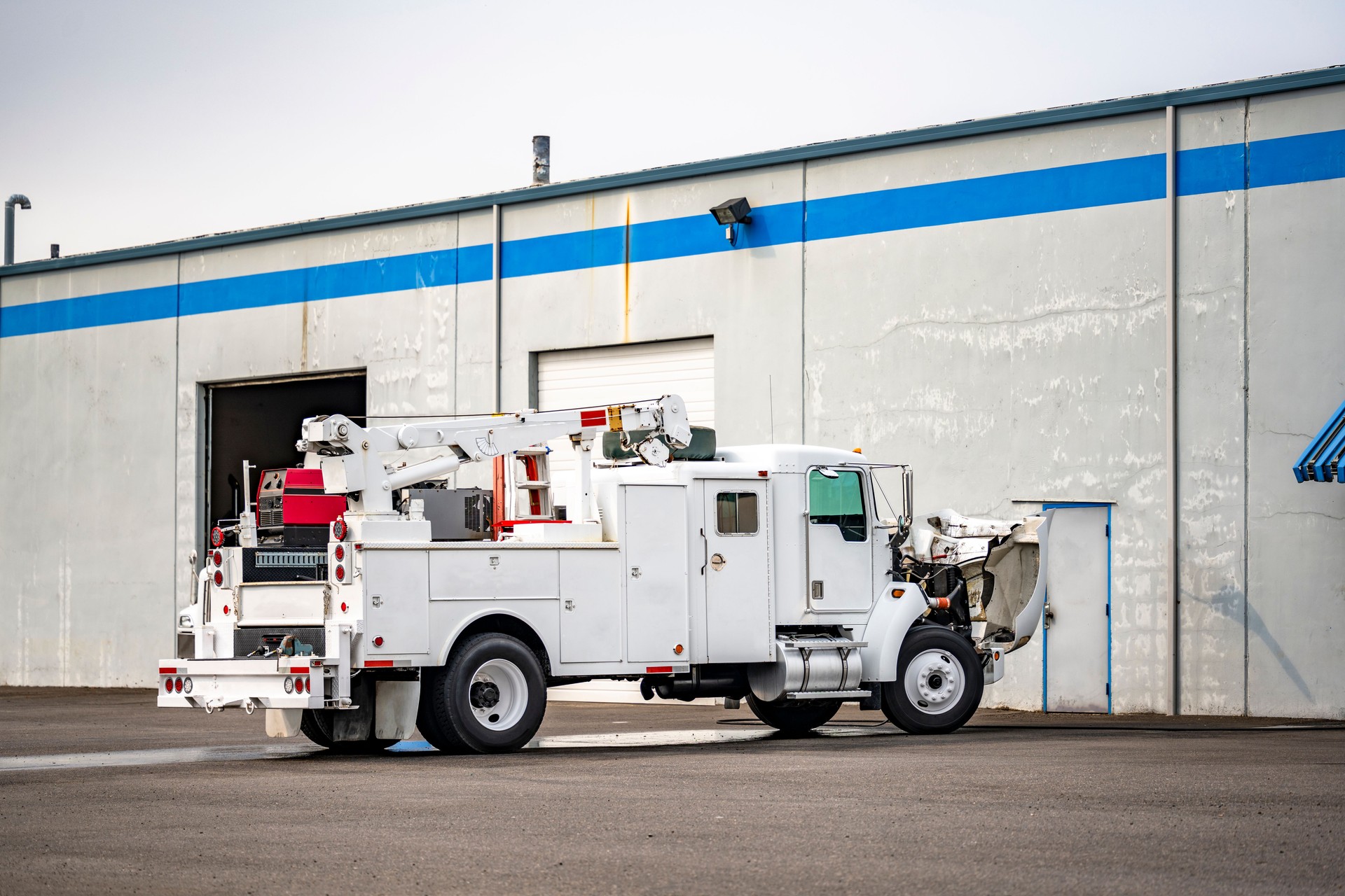 Powerful semi truck equipped with crane and welding machine for mobile repair of broken vehicles on the road stands with an open hood in a parking lot near a warehouse for maintenance